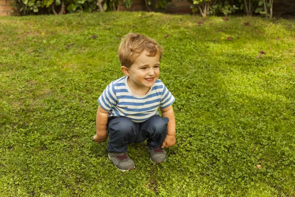 Tiro completo retrato bonito sorridente bebê menino agachamento na grama — Fotografia de Stock