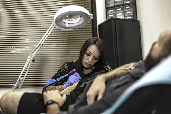 Professional woman tattooer working tattoo in a man leg. — Stock Photo, Image