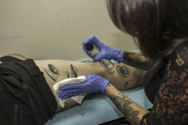 Close up professional woman tattooer cleaning tattoo in a man le — Stock Photo, Image