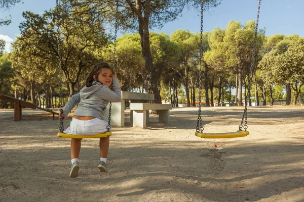 Vista posteriore ragazza sorridente divertirsi sull'altalena al parco giochi — Foto Stock