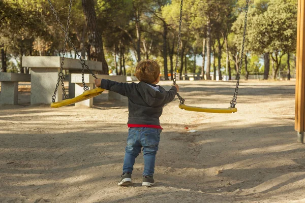 Visão traseira menino se divertindo com o balanço no playground — Fotografia de Stock