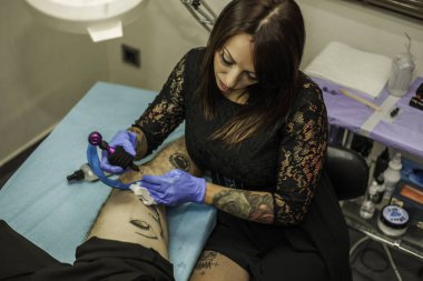 Profesyonel kadın tattooer bir adam bacak çalışma dövme. Yüksek bir