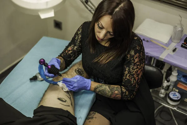 Professionell kvinna tattooer arbetande tattoo i en man ben. Hög en — Stockfoto