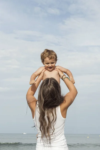 Giovane donna da dietro che indossa una maglietta bianca con in braccio un bambino. A — Foto Stock