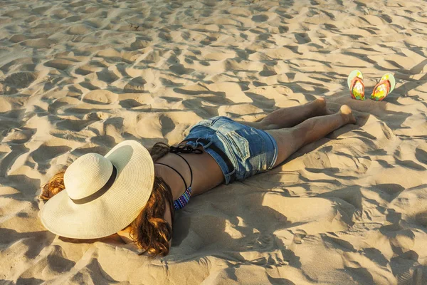 Chica acostada en la playa con sombrero de verano de playa y chancla . — Foto de Stock
