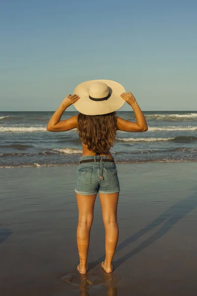 Mujer joven por detrás, con sombrero de playa de verano y pantalones cortos jea — Foto de Stock