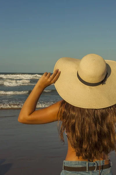 Mujer joven por detrás, con sombrero de playa de verano y pantalones cortos jea — Foto de Stock