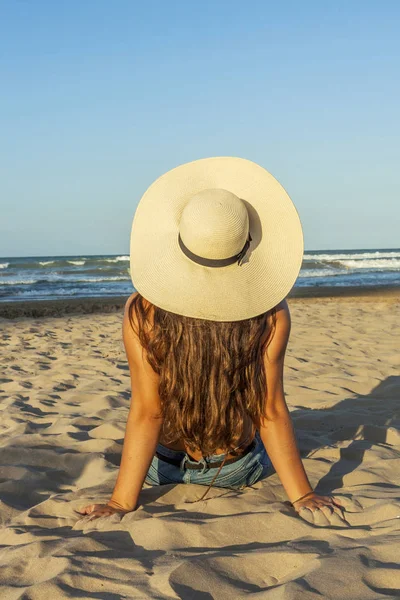 Young woman from behind, long hair, wearing summer hat in the be