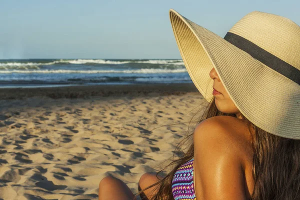 Chica sentada en la playa con sombrero de verano playa convertido admiri — Foto de Stock