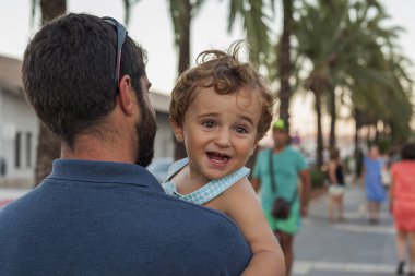 Arka görünümü adam erkek gülümseyen bir bebek tutan. Yaz plaj yer.