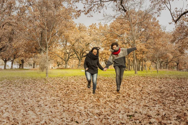 Young women running in the park over a field full of leaves. Aut — Stock Photo, Image