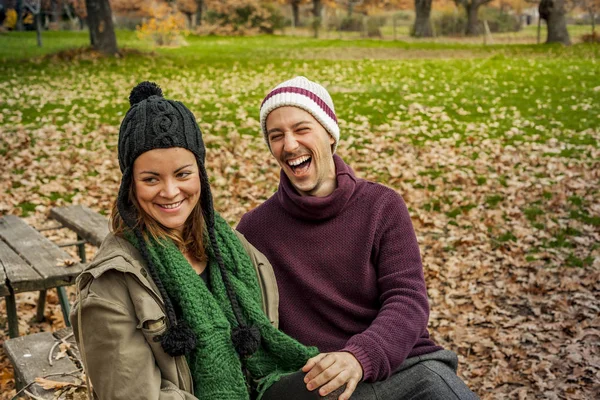 Hermosa pareja joven hablando, sentarse en un banco en el parque en autum —  Fotos de Stock