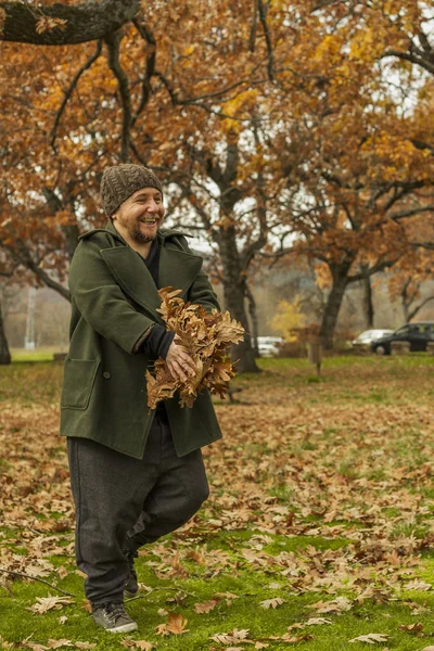 Retrato homem rindo com chapéu de lã brincando com folhas. Outono — Fotografia de Stock