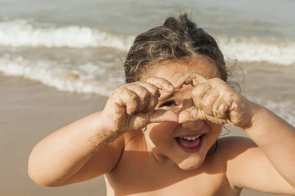 Ragazza che guarda attraverso un cuore disegnare con le mani. Spiaggia. Estate — Foto Stock