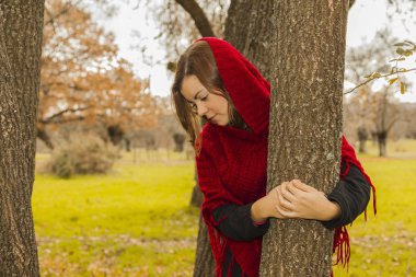 Bir ağaç gövdesine sarılma kırmızı yün panço giyen kadın. Natur