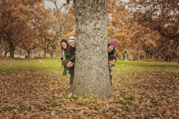 Grupo de jóvenes escondidos detrás de un árbol. Paisaje otoñal — Foto de Stock