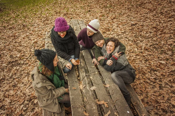 Amigos riéndose se sientan en un banco de madera del parque. Otoño . — Foto de Stock