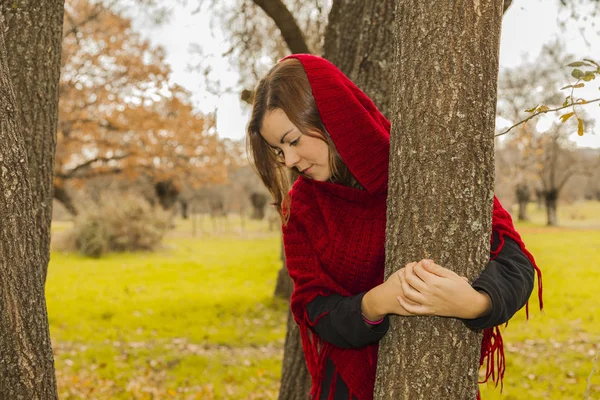 Mujer con poncho de lana roja abrazando el tronco de un árbol. Natur. — Foto de Stock