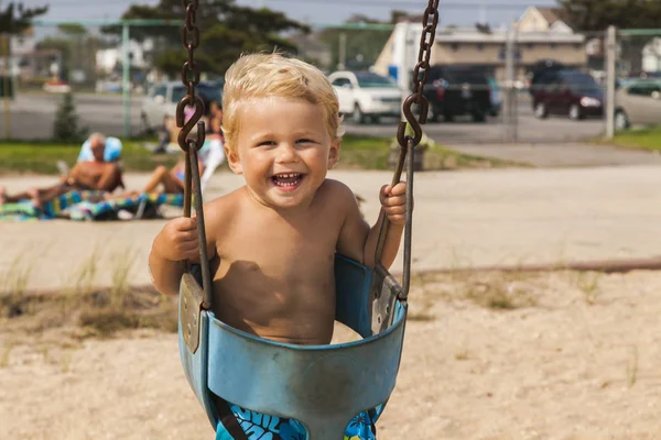スイングの遊び場で楽しんで幸せな男の子。夏 — ストック写真