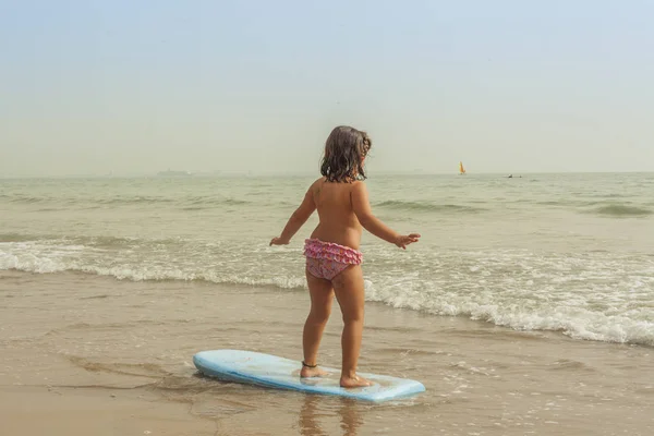 背面ビュー女の子練習サーフボード、ビーチの海岸で. — ストック写真