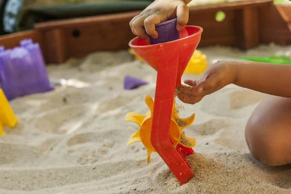 Händerna kasta sand i en plast mill leksak i en sandlåda. Rörelse — Stockfoto
