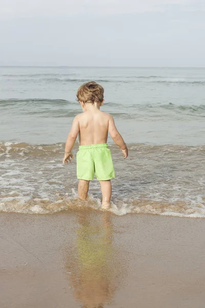 背面ビュー少年がビーチの海岸で水着を着ています — ストック写真