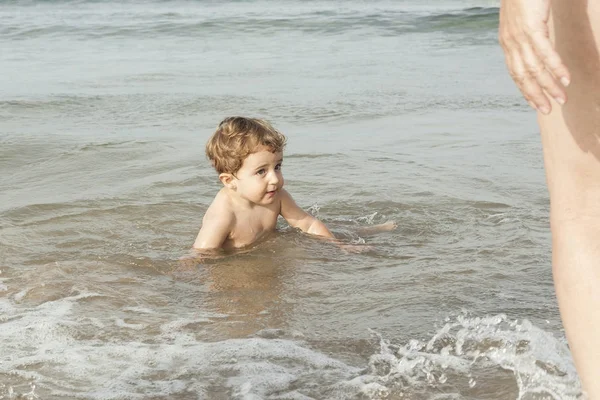 彼の母親を見てビーチの海岸で泳いでいる赤ちゃん少年 — ストック写真