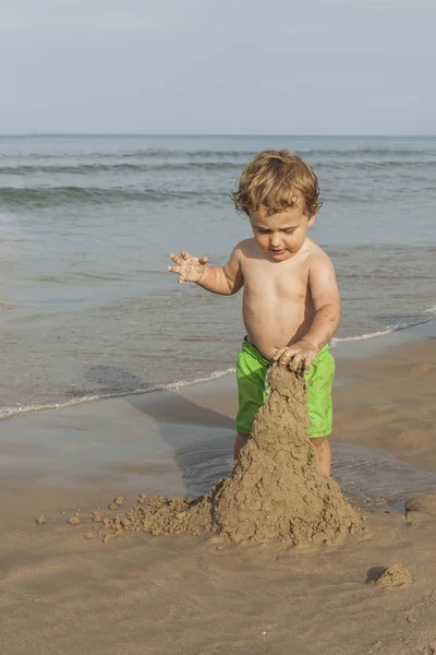 ビーチの海岸で砂の塔をやって水着を身に着けている男の子 — ストック写真