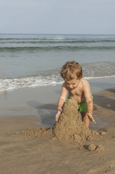 ビーチの海岸で砂の塔をやって水着を身に着けている男の子 — ストック写真