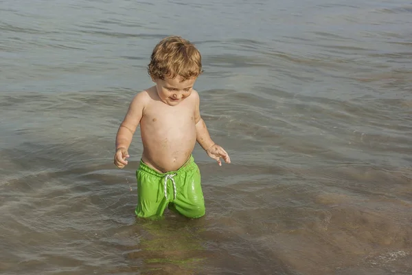 ビーチの海岸で遊ぶ水着を身に着けている男の子 — ストック写真