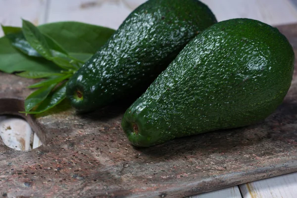 Gröna mogna avokado med lämnar på granit planka — Stockfoto