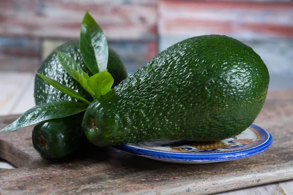 Gröna mogna avokado med lämnar på granit planka — Stockfoto