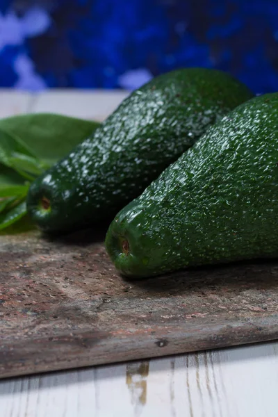 Gröna mogna avokado med lämnar på granit planka — Stockfoto