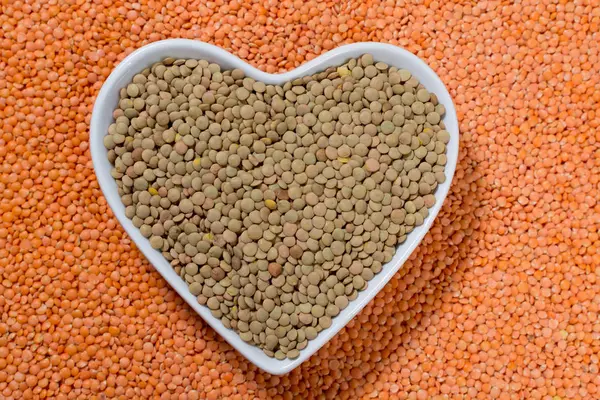 Heart form bowl with green lentils over red lentils background - healthy food concept