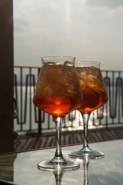Waiter prepared the Aperol Sprits summer cocktail with Aperol, prosecco, ice cubes and orange in wine glass, ready to drink on sunny terrace with sea view