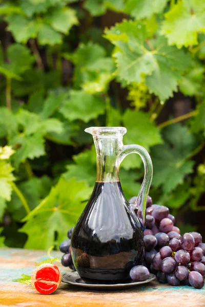 Черный старый бальзамический уксус в стакане со свежим красным виноградом — стоковое фото