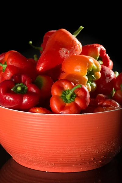 Red bowl with fresh ripe red sweet paprika on black background with reflection, copy space