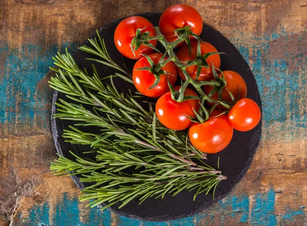 Red cherry tomatoes on vine and fresh green rosemary top view — Stock Photo, Image