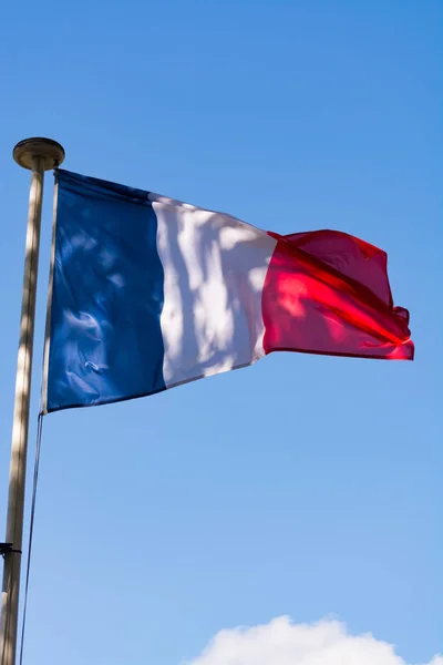 Flag of France is a tricolour flag featuring three vertical bands coloured blue (hoist side), white, and red. Oudoors, blue sky, copy space.