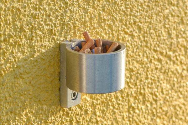 Caixa de cigarros de aço inoxidável montada na parede exterior, fora de um local de trabalho, onde o fumo é proibido no interior. Isso permite que os fumantes apaguem e descartem cigarros . — Fotografia de Stock