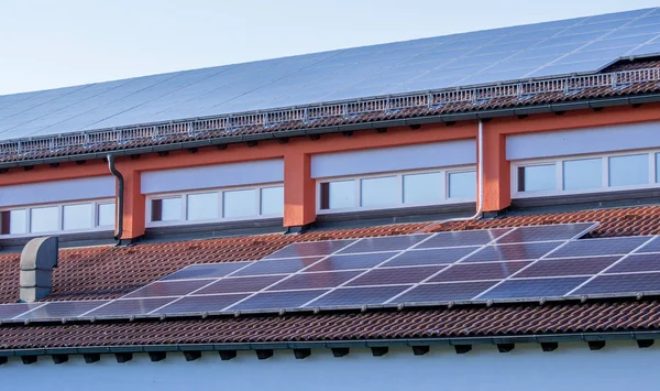 Painel solar em um telhado vermelho que reflete o sol eo céu azul sem nuvens — Fotografia de Stock