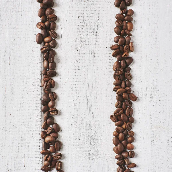 Coffee roasted brown beans on a white wooden background in the form of tracks or pauses