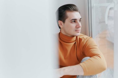 Genç bir adam pencerede oturuyor ve sokağa bakıyor.