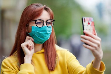 Tıbbi maskeli bir kız eliyle ayarlar, cep telefonu tutar, video bağlantısı ile konuşur ya da selfie çeker.
