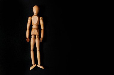 Siyah arka planda tahta kukla. Boş bir siyah arka planda, rahat bir şekilde yaslanmış tahta bir adam. Uzun boylu tahta bir adamın heykeli.