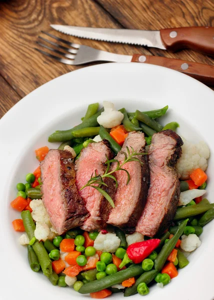 Sliced Beef steak medium rare with asparagus beans,cauliflower,carrot and pea on wooden table.closeup selective focus.Fork and knife — Φωτογραφία Αρχείου