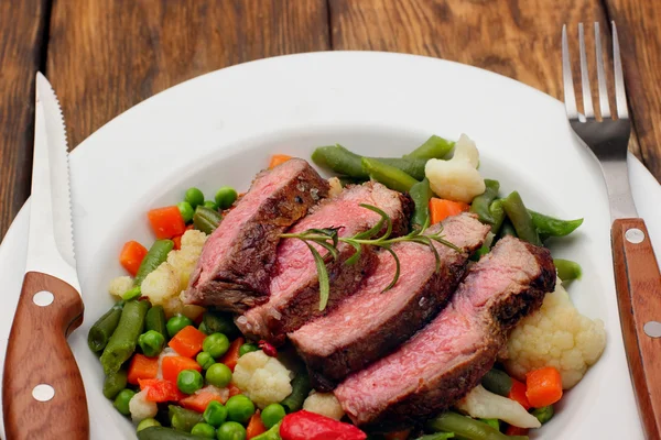Sliced Beef steak medium rare with asparagus beans,cauliflower,carrot and pea on wooden table.closeup selective focus.Fork and knife — Stock Photo, Image