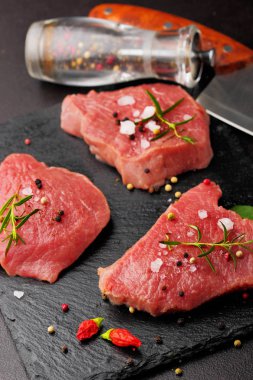 Taze çiğ dana biftek Mignon, tuz, karabiber, biberiye, pepepr biber ile. Karanlık masanın üstünde. Uzay kopyalayın. Seçici odak. İkinci plan üzerinde Pepepr değirmen ve bıçak decosued