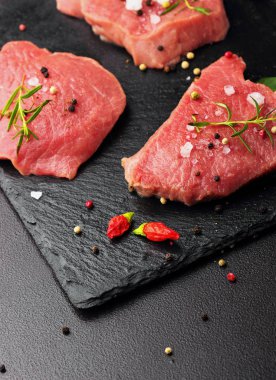 Taze çiğ dana biftek Mignon, tuz, karabiber, biberiye, pepepr biber ile. Karanlık masanın üstünde. Uzay kopyalayın. Seçici odak