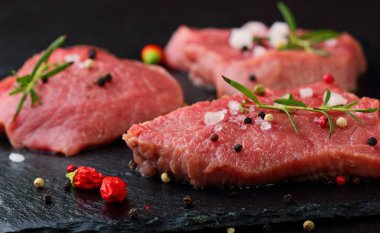 Taze çiğ dana biftek Mignon, tuz, karabiber, biberiye, pepepr biber ile. Karanlık masanın üstünde. Uzay kopyalayın. Seçici odak